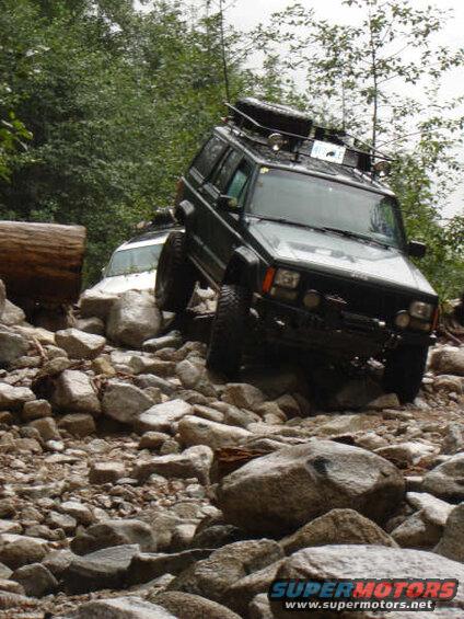 Dark Jeep Cherokee driving over large rocks on an off-road trail.