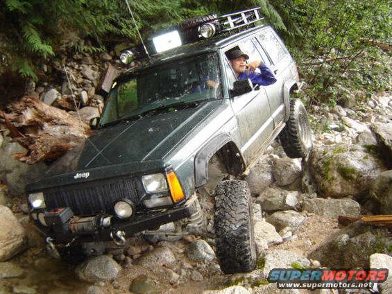 Green Jeep Cherokee off-roading over large rocks.