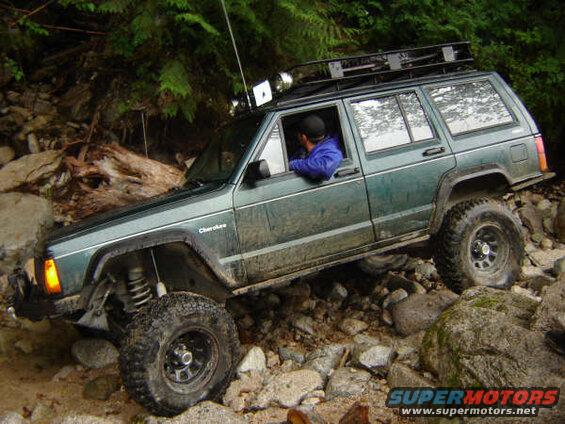 Green Jeep Cherokee off-roading on a rocky trail.