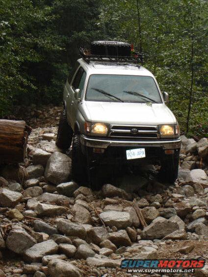 Silver SUV on a rocky trail with a roof rack and spare tire.