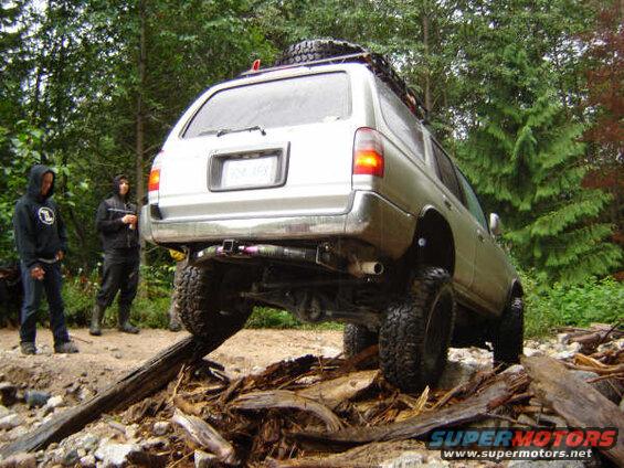 Silver SUV on a challenging off-road trail with two people watching.