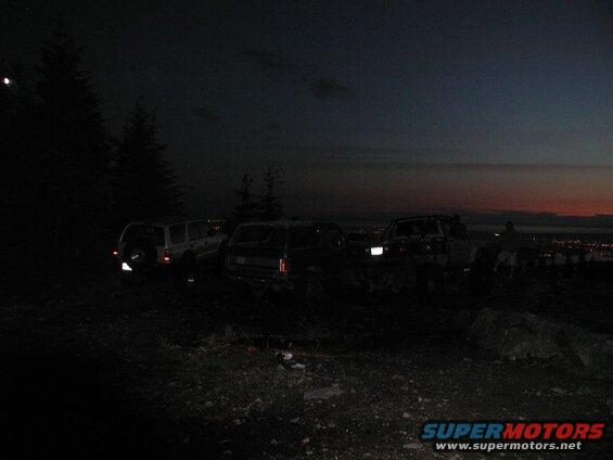 Off-road vehicles parked on a hill overlooking a city at dusk.