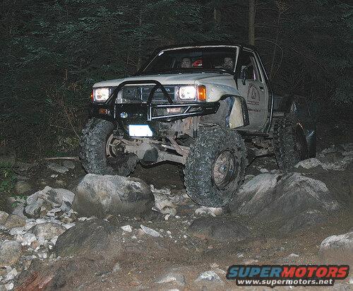 Lifted pickup truck with large off-road tires on a rocky trail at night.