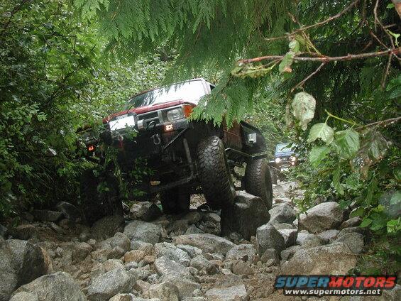 Red off-road vehicle on a rocky trail surrounded by trees.
