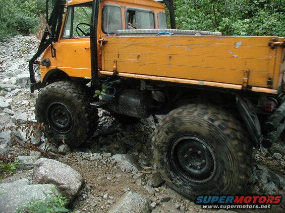 Orange Unimog truck driving over rocks on an off-road trail.