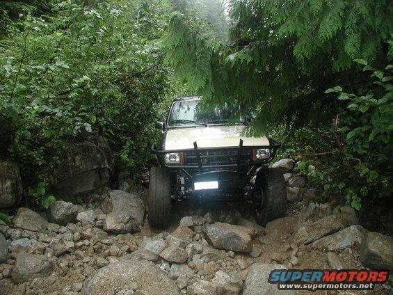 Off-road vehicle on a rocky trail surrounded by trees.