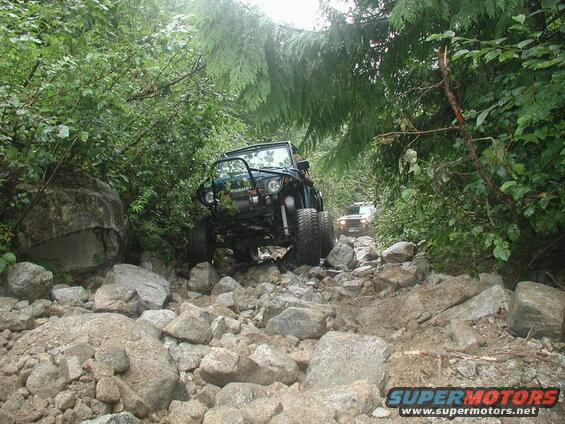 Suzuki Samurai driving on a rocky forest trail.