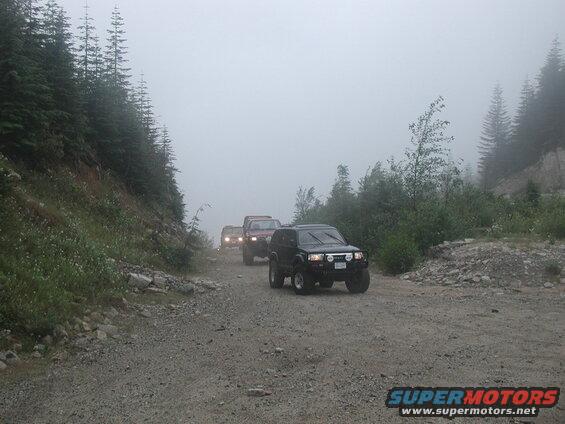 Four-wheel drive vehicles on a foggy gravel mountain road.