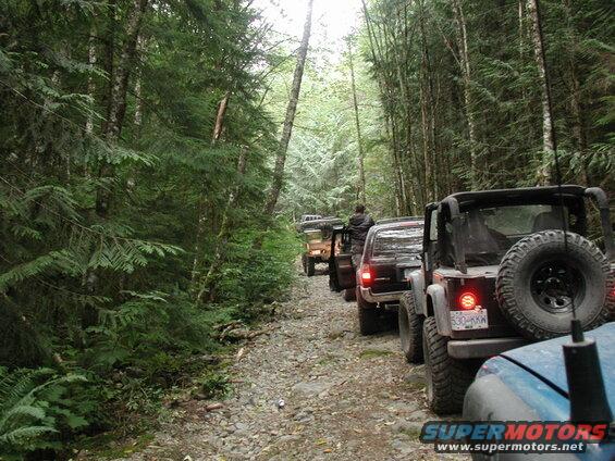 Several off-road vehicles driving down a rocky, wooded trail.