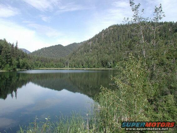 A serene lake with reflections of forested hills under a partly cloudy sky.
