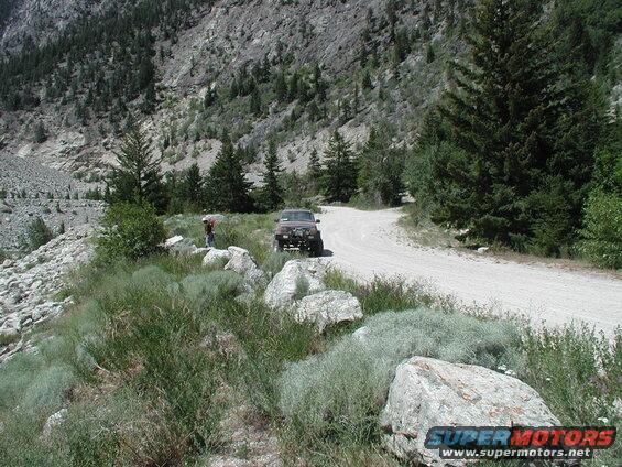 Dark SUV parked on a dirt road with a person standing nearby.