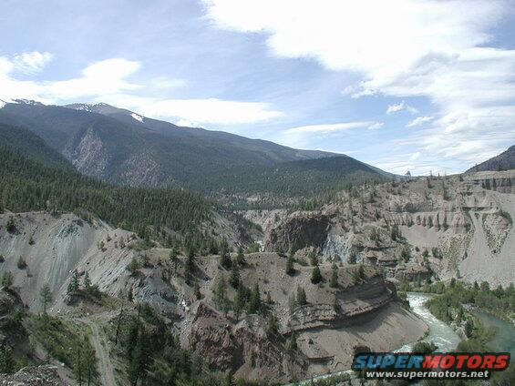 River flowing through a canyon with eroded cliffs and forested mountains.