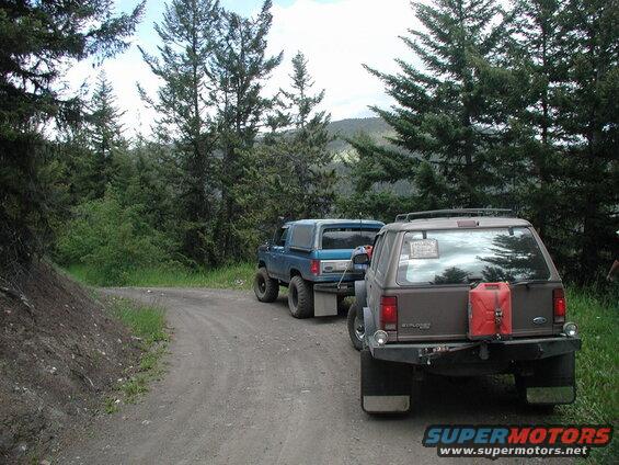 Brown Ford Explorer and blue Ford Bronco on a dirt road in a forest.