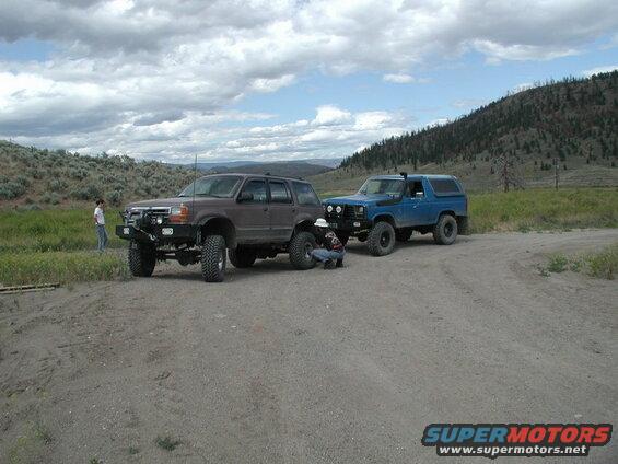 Blue 1985 Ford Bronco with lifted suspension and off-road tires, parked on a dirt road.