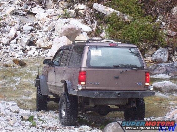 Lifted brown Ford Explorer driving through a rocky stream.