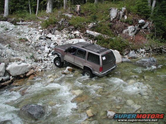 Lifted brown SUV driving through a rocky stream.