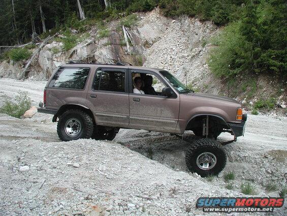 Lifted brown Ford Explorer off-roading on a rocky trail.