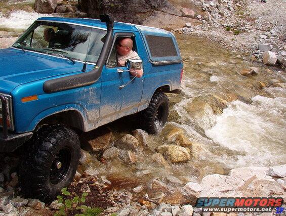 Blue Ford Bronco driving through a rocky stream with a snorkel.