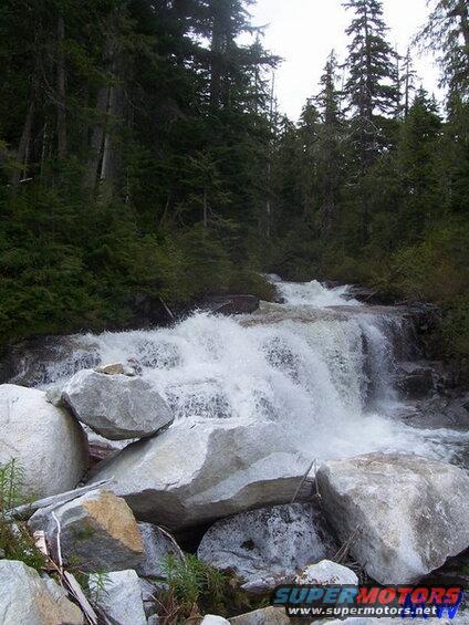 Waterfall in a forest with large rocks in the foreground.