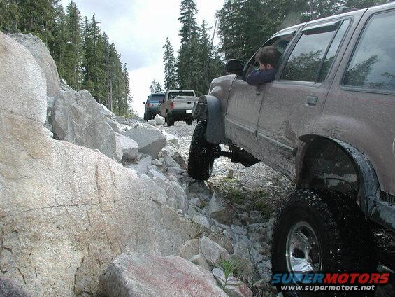 Brown SUV on a rocky off-road trail with other vehicles.