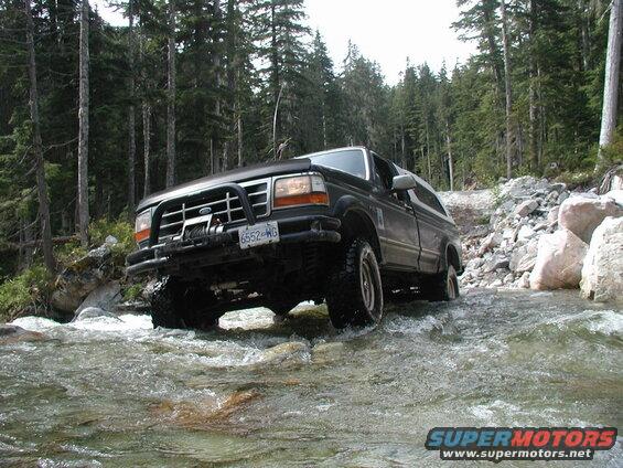 Dark Ford Bronco driving through a river in a forest