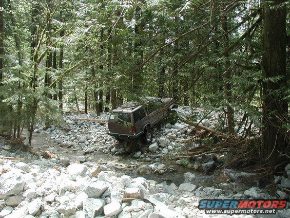 Brown SUV stuck in a rocky streambed in a forest.
