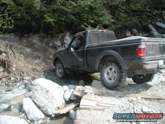 Black pickup truck driving through a rocky stream.