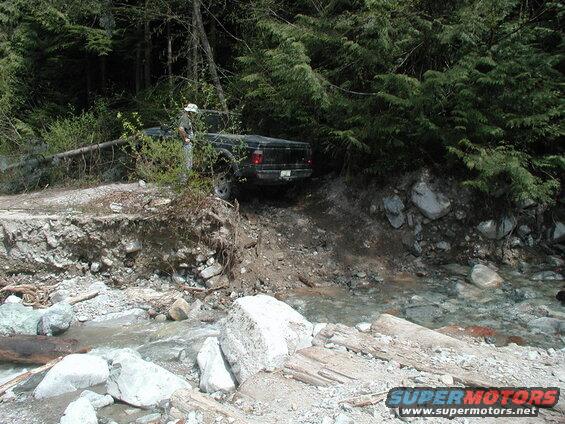 Person standing next to a black pickup truck on a damaged road.