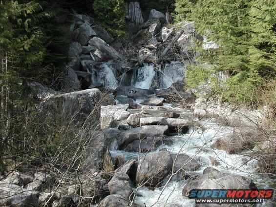 A rocky stream with a small waterfall flowing through a forest.