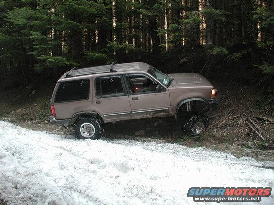 Lifted tan Ford Explorer on a snowy forest trail.