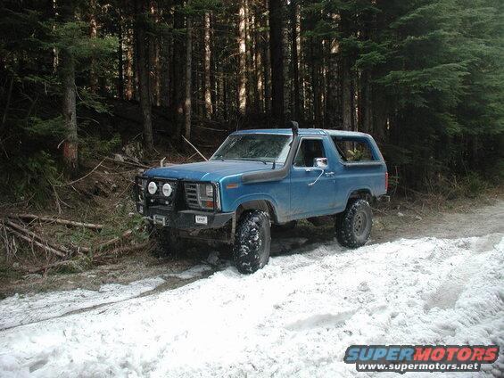 Blue Ford Bronco with off-road modifications on a snowy forest trail