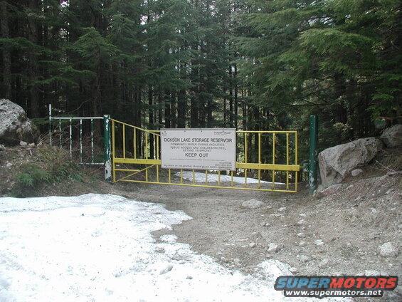 Yellow gate with a sign blocking a forest road.