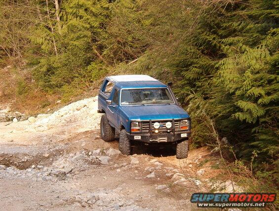 Blue 1985 Ford Bronco on a rocky trail with trees