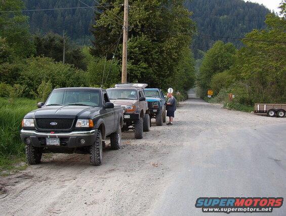 Several off-road trucks and SUVs parked on a gravel road.