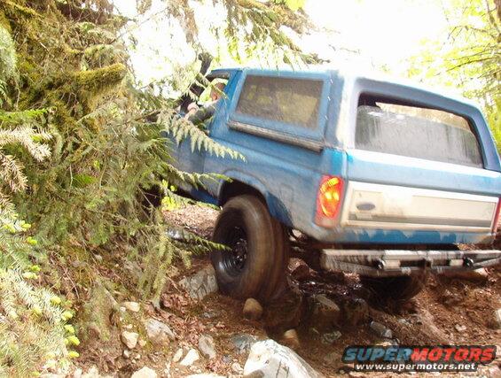 Blue Ford Bronco off-roading on a rocky, wooded trail.