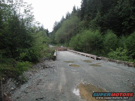 Gravel road and wooden bridge in a forest with debris.