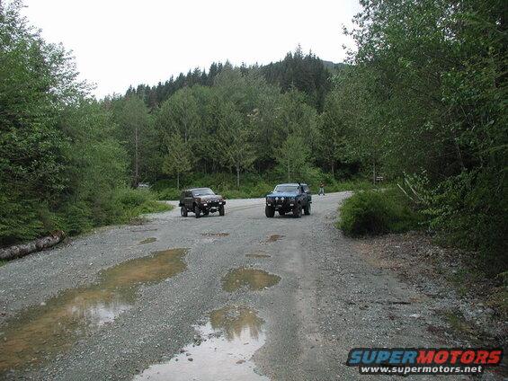 Two SUVs on a gravel road in a forest.