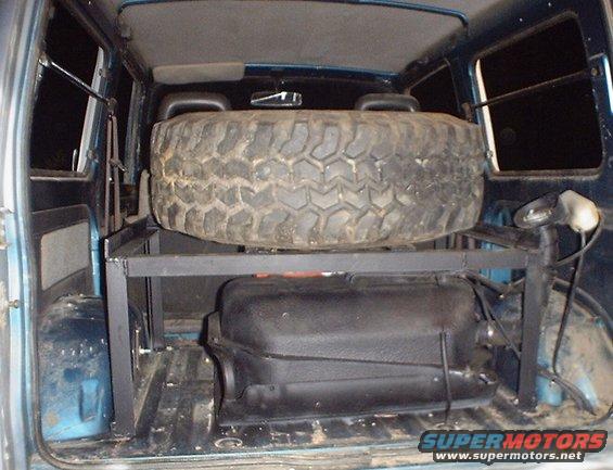 Spare tire mounted above a fuel tank inside a vehicle's cargo area
