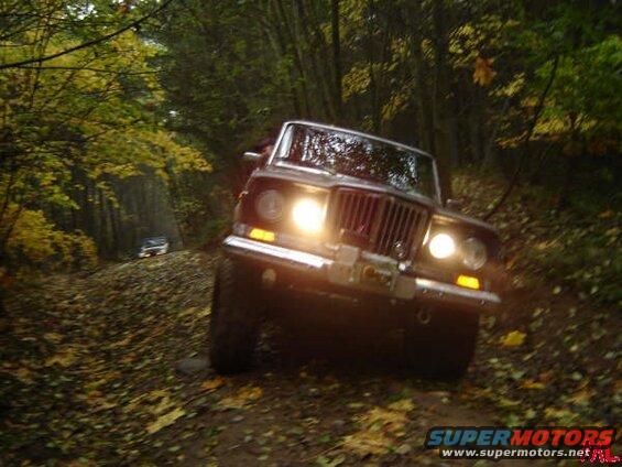 Dark Jeep Cherokee driving on a dirt path in a forest during autumn.