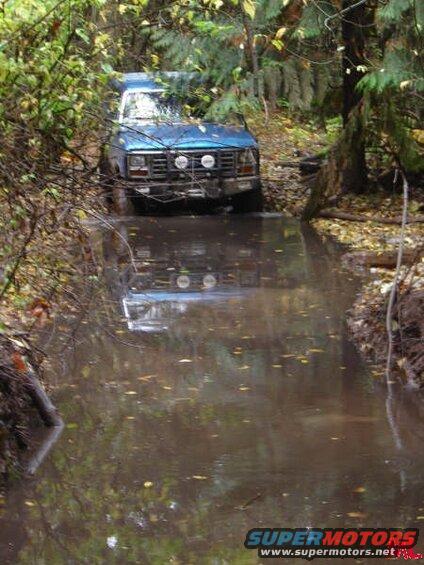 Blue SUV driving through a muddy path in a forest.