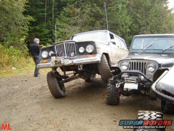 Two off-road Jeeps parked on a dirt road in a forest.