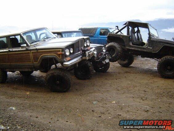 Lifted Jeep Wrangler and wood-paneled station wagon parked on dirt.