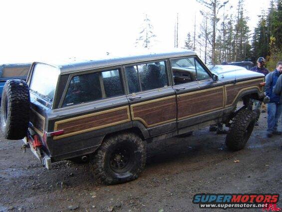 Lifted Jeep Grand Wagoneer with wood paneling on dirt road, spare tire on rear.