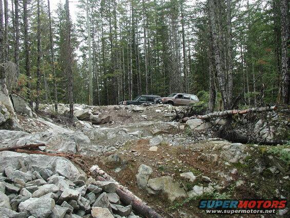 Two SUVs on a rocky, wooded trail.