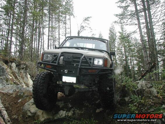 Tan off-road pickup truck with custom bumper and large tires on a rocky trail.