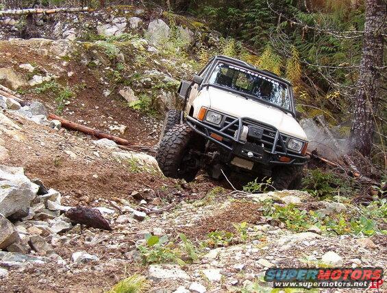 Tan off-road vehicle with brush guard climbing a steep, rocky trail.