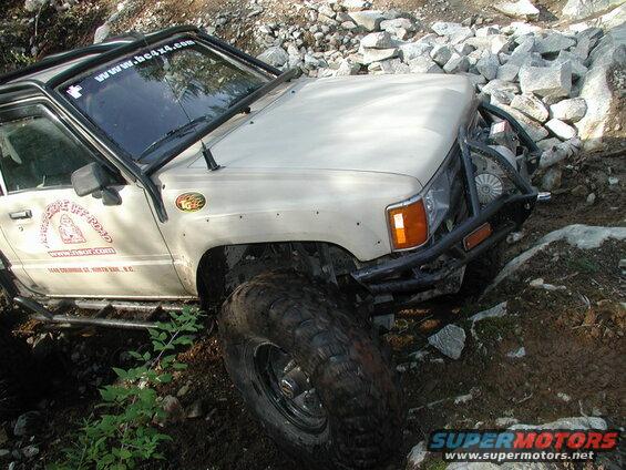 Beige off-road SUV on rocky terrain with custom roll cage and large tires.