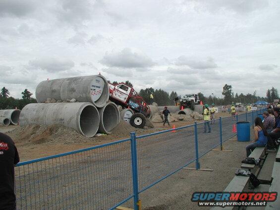 Modified truck on concrete pipes with flames, another SUV in background.
