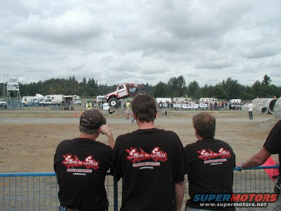 Monster truck jumping over a dirt mound with spectators watching.