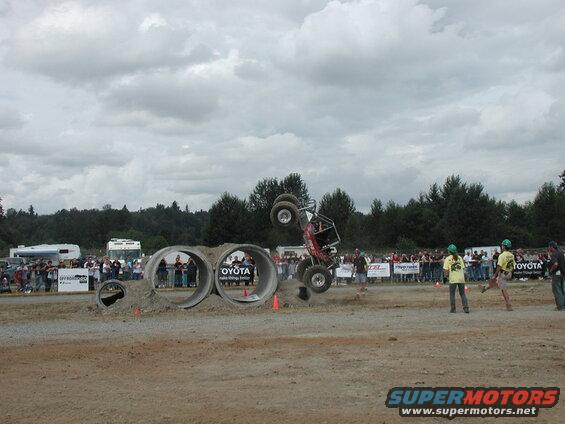 Off-road buggy flipping over concrete pipes with spectators watching.